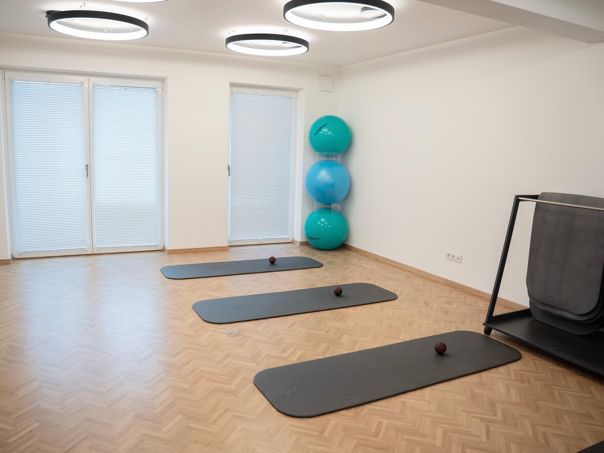 Fitnessraum mit drei Matten, Bällen und großen Fitnessbällen in der Ecke. Beleuchtung durch runde Deckenleuchten.