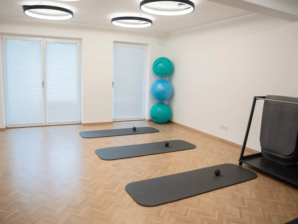 Fitnessraum mit drei Matten, Bällen und großen Fitnessbällen in der Ecke. Beleuchtung durch runde Deckenleuchten.