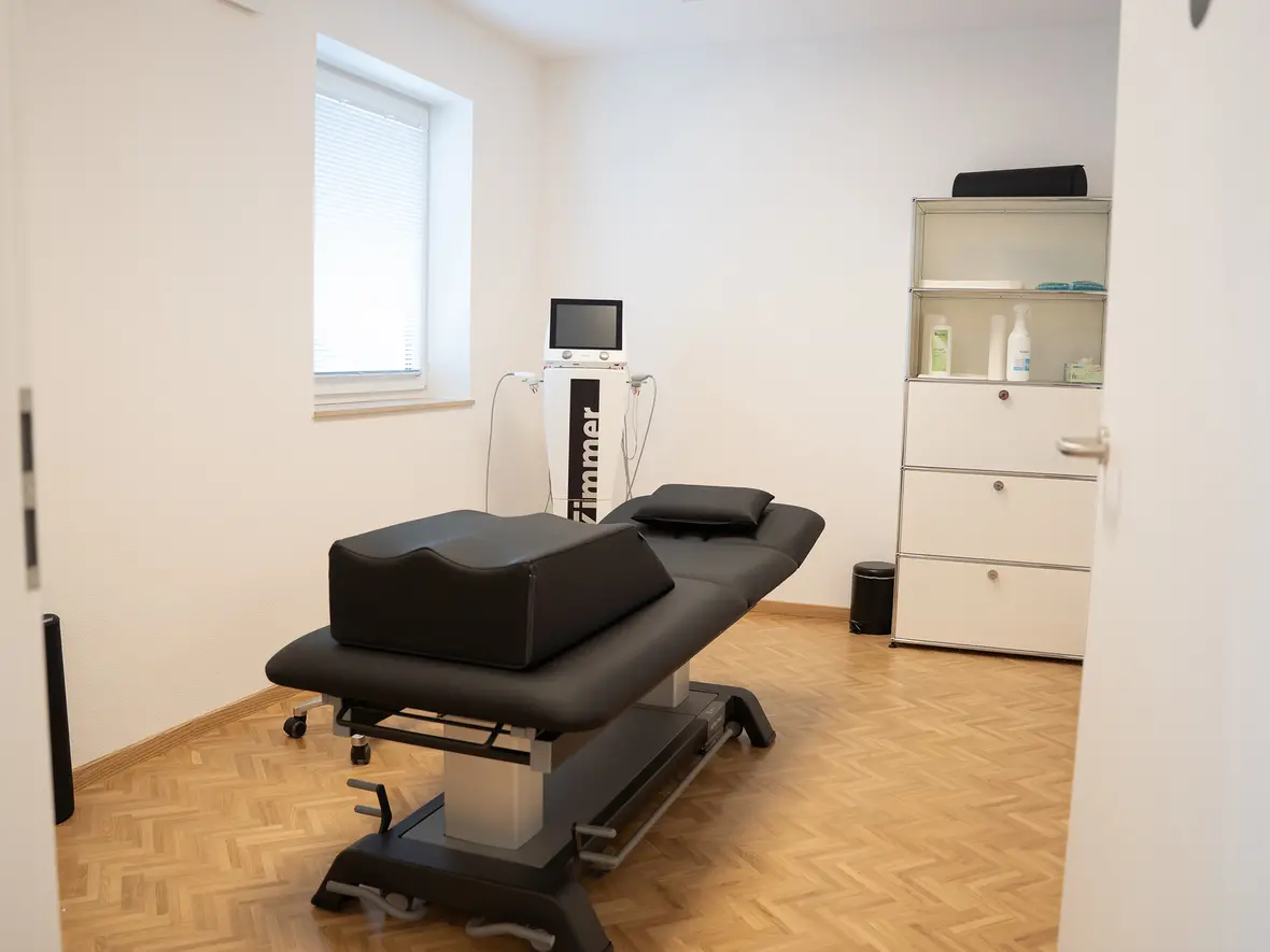 Therapieraum mit Behandlungsliege, Regal und medizinische Utensilien.