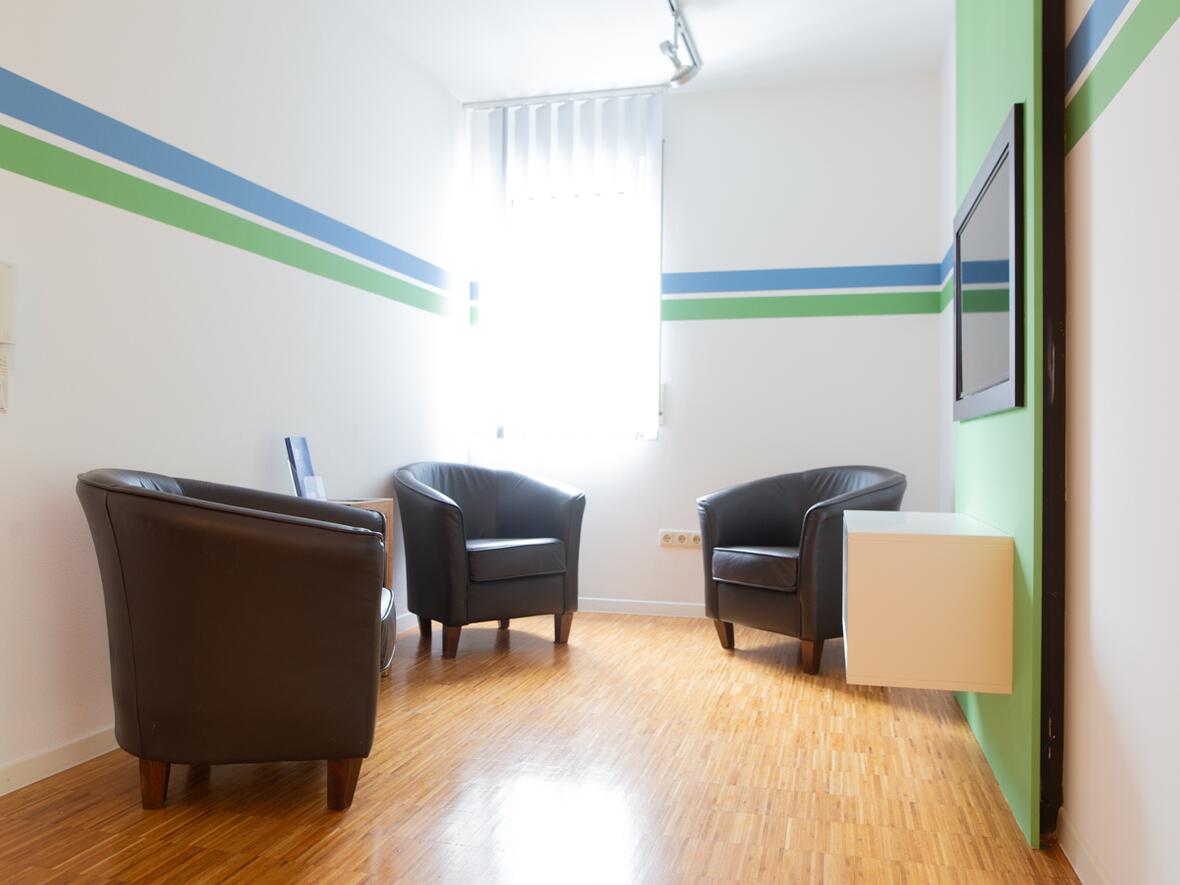 Heller Wartebereich der Physiotherapie Bartochek mit drei dunklen Ledersesseln, Holzboden und Wandgestaltung in Grün und Blau.