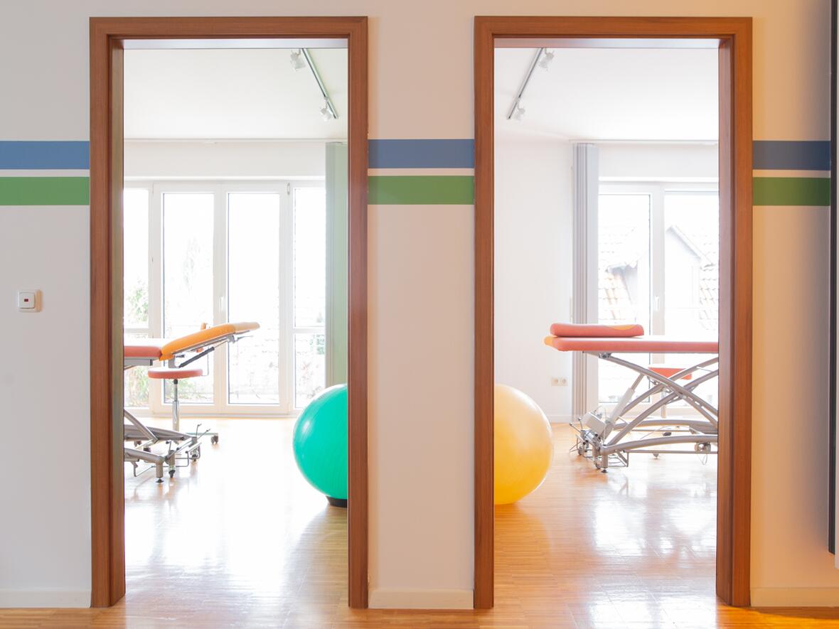 Zwei helle Behandlungsräume der Physiotherapie Bartochek mit orangefarbenen Therapieliegen und bunten Gymnastikbällen, durch offene Türen sichtbar.